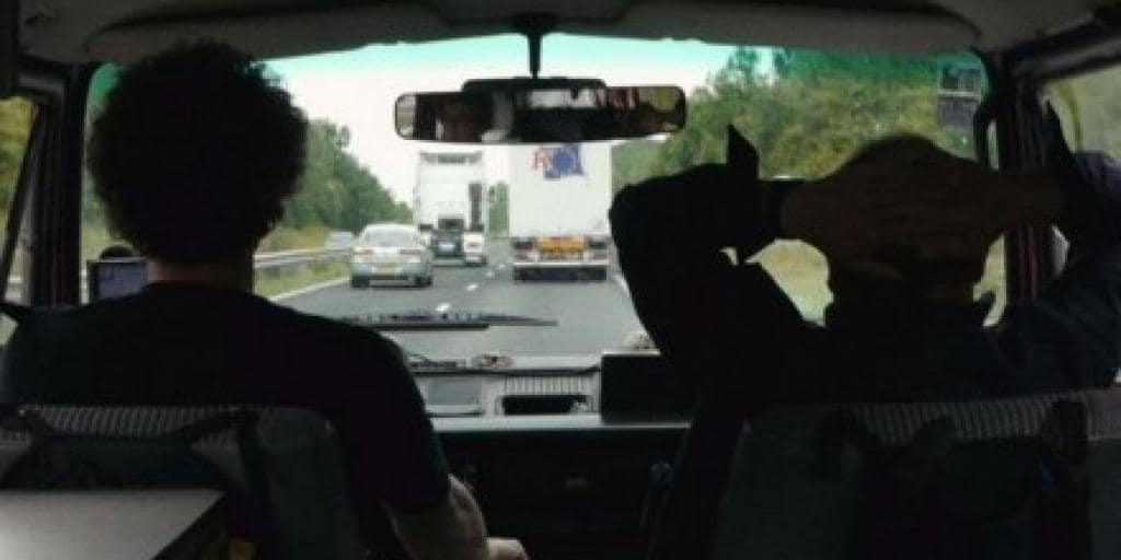 ALT - Wnętrze samochodu z tylnego siedzenia. Na przednich siedzą mężczyźni. Przed pojazdem droga z innymi samochodami.