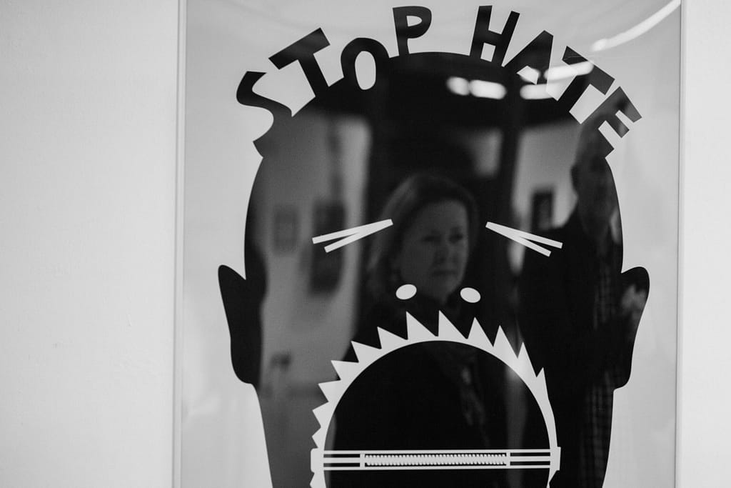 ALT - Rysunek maski człowieka z zamkniętymi oczami i szeroko otwartymi ustami. Na górze maski napis: stop hate.