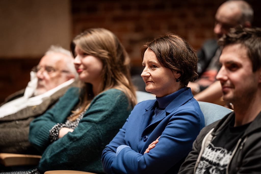 Publiczność na fotelach. Patrzą w stronę sceny. Uśmiechają się.