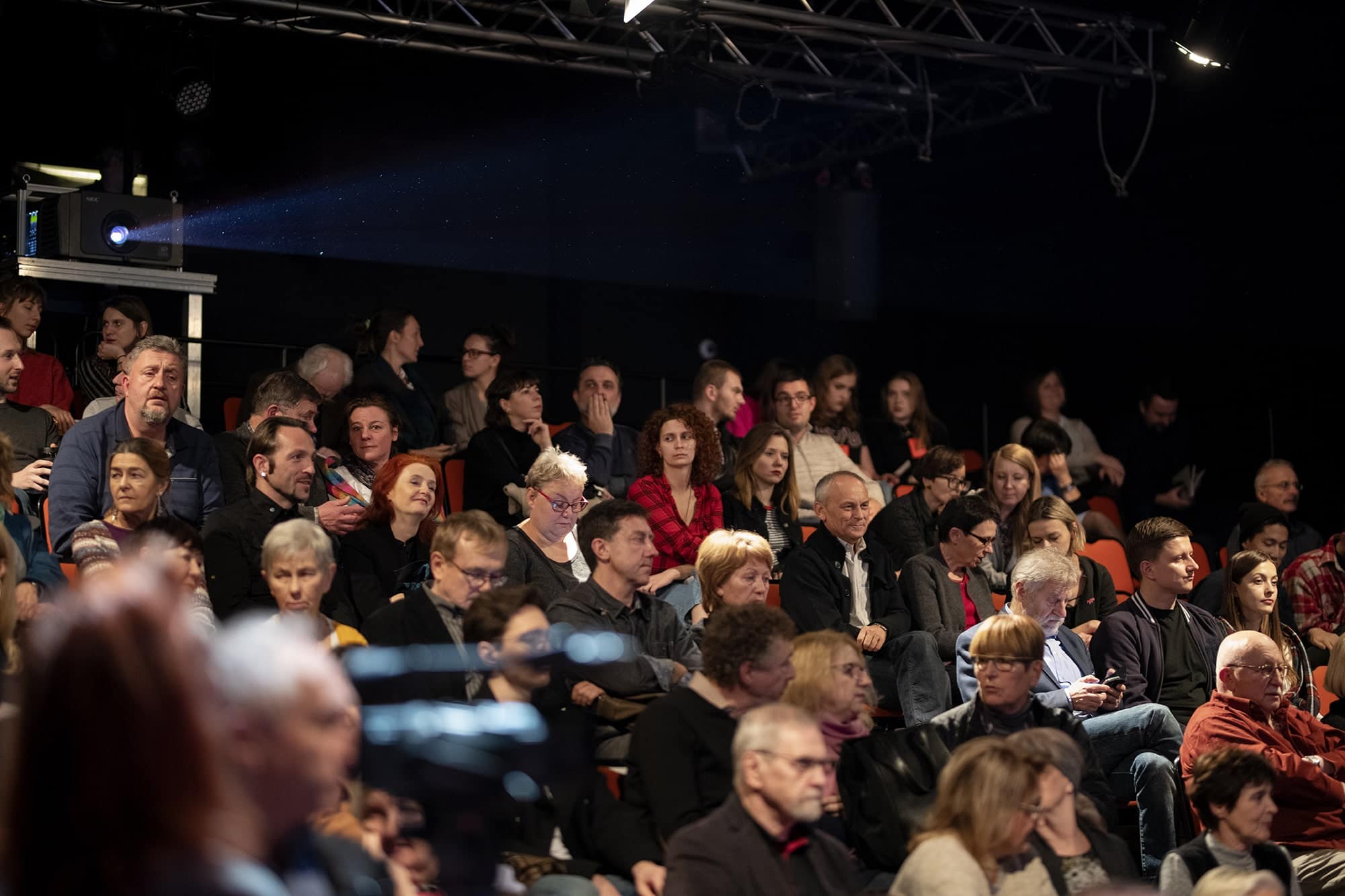 ALT - Widok ogólny z boku na kilkadziesiąt osób siedzących na sali kinowej.